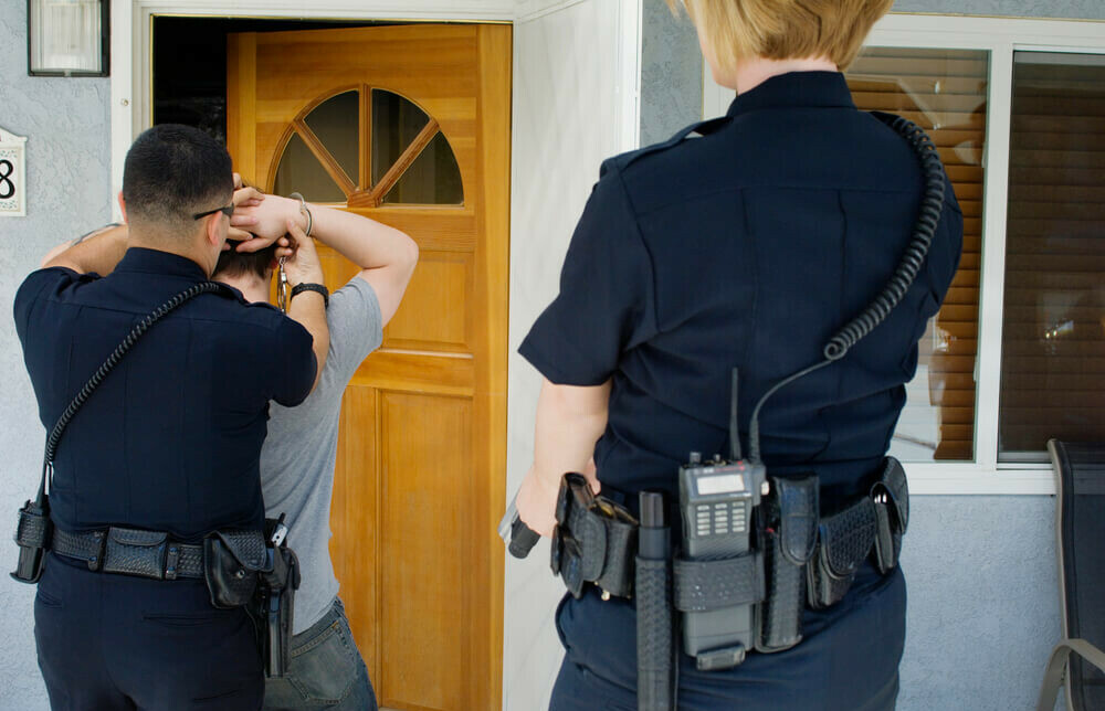 police arresting man at the door to a home